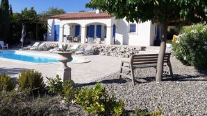 A poolside area with lounge chairs, a stone fountain, and a building with blue shutters. - Modern Villa in Camplong With Private Pool (Felines-Minervois)