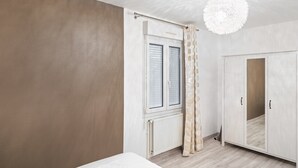 Un dormitorio con cama, armario, ventana con cortinas y lámpara colgante.