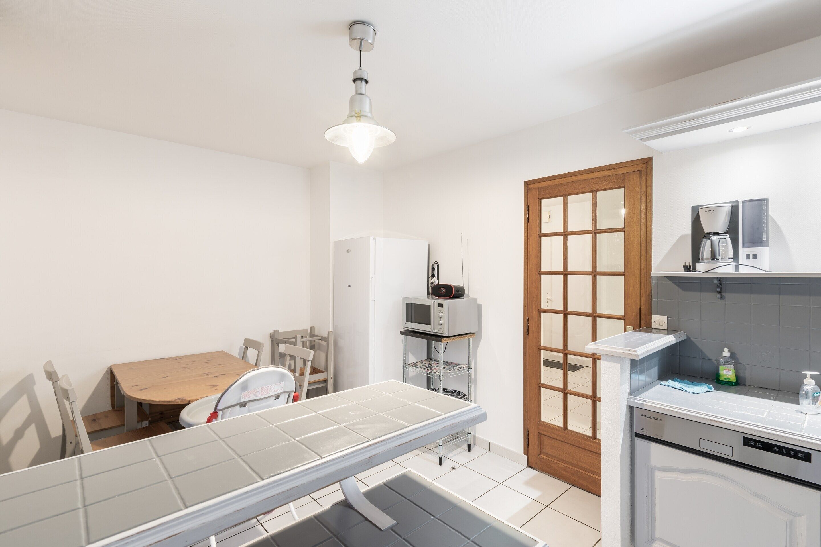 A compact kitchen with a dining table, chairs, a microwave, a coffee maker, and a dishwasher.