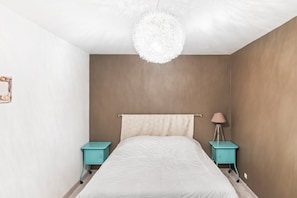 Une chambre à coucher comprenant un lit, deux tables de chevet, un luminaire suspendu et une lampe fixée au mur.