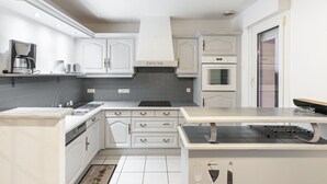 Una cocina moderna con armarios blancos, horno empotrado y cafetera.