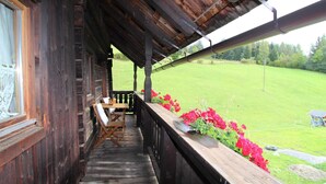 A wooden porch with a table and chairs, overlooking a green field. - Farmhouse in Fresach Near Millstatt Lake (Fresach)