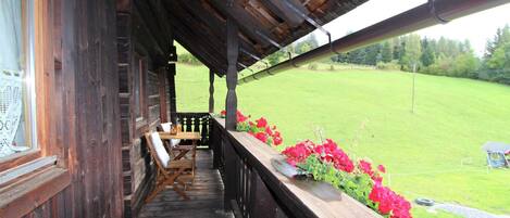 A wooden porch with a table and chairs, overlooking a green field.