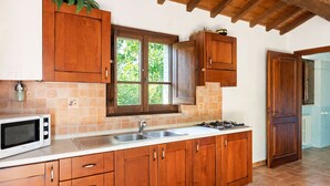 A kitchen with wooden cabinets, a microwave, a sink, and a window with a view of greenery. - Tranquil Stay in the Heart of Umbria (Città di Castello)