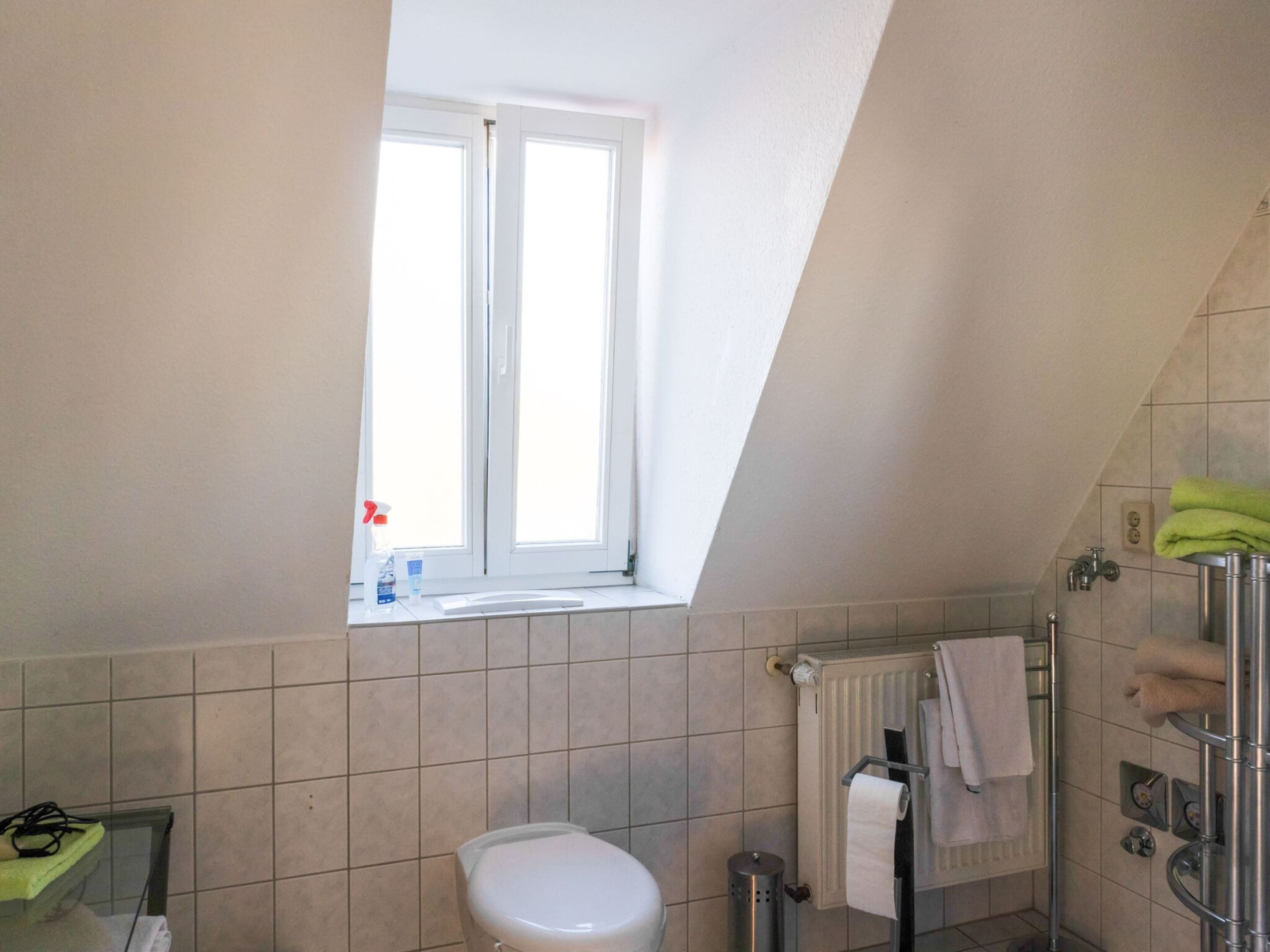 A bathroom with a toilet, a window, a radiator, and a shower area.