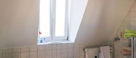 A bathroom with a toilet, a window, a radiator, and a shower area.