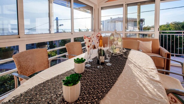 A dining area with a table set for two, large windows, and a view of the cityscape. - Beautiful Holiday Home in Maslenica Near Beach" (Jasenice)