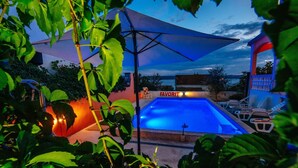 A swimming pool with a blue-lit interior, surrounded by greenery and a covered area with a 'FAVORIT' sign. - Beautiful Holiday Home in Maslenica Near Beach" (Jasenice)
