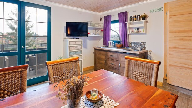 Une cuisine chaleureuse avec une table en bois, des chaises en osier et un téléviseur.