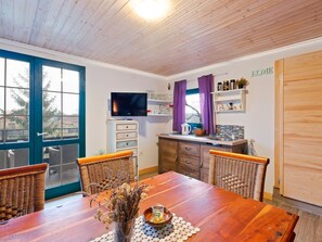 Une cuisine chaleureuse avec une table en bois, des chaises en osier et un téléviseur.