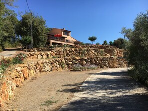 A stone retaining wall with a paved path, a building with a red roof, and surrounding greenery. - Villa in Provence With Pool and Vineyard Views (Saint-Antonin-du-Var)