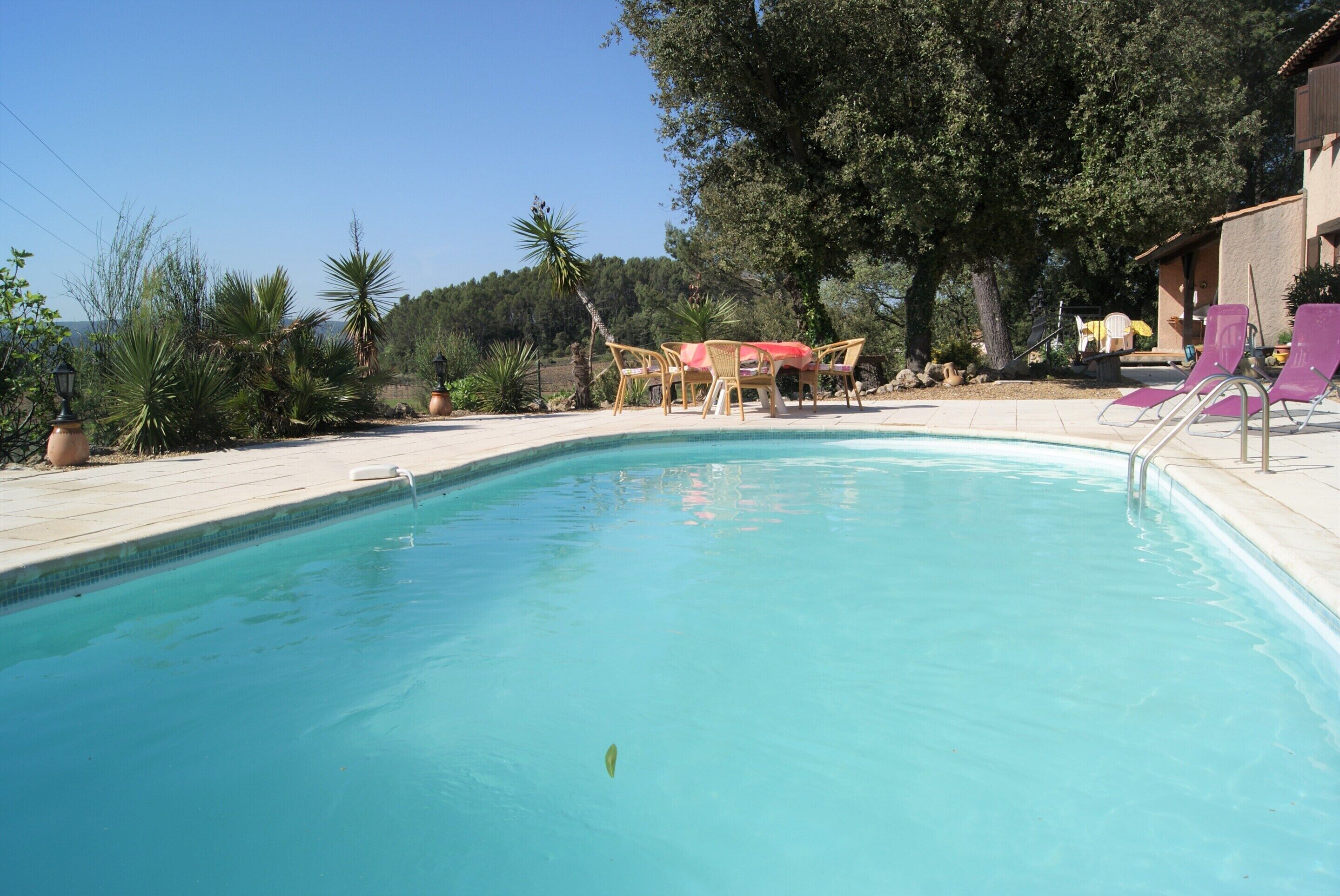 A swimming pool with lounge chairs and a table, surrounded by trees and a building.
