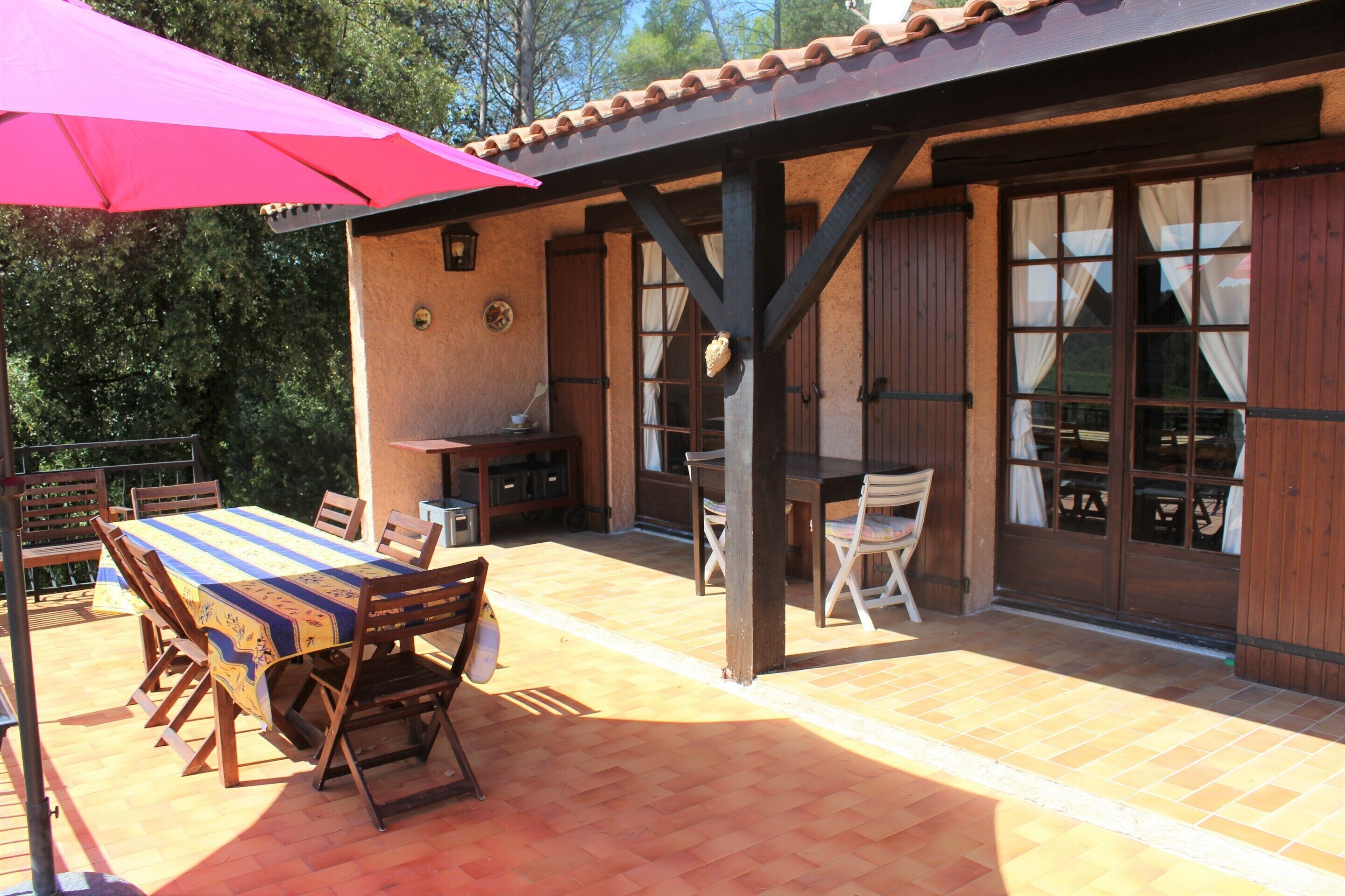 Un patio al aire libre con una mesa, sillas, una parrilla y un área cubierta con ventanas.