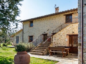 A stone building with a staircase leading to a wooden door, a bench, and a potted plant in the foreground. - Holiday Home Near Pietrafitta Lake (Piegaro)