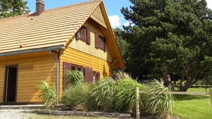 Un edificio de madera amarillo con techo de tejas, una chimenea y una puerta con la leyenda 'GITE AU ROCHER 16A'.