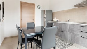 A modern kitchen with a dining area, featuring a wooden door, a clock, a refrigerator, and a sink. - Belvilla by OYO Appartamento Monferrato (Albugnano)