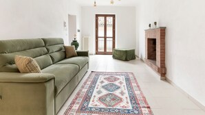 A living room with a green sofa, a patterned rug, a fireplace, and hanging light bulbs. - Belvilla by OYO Appartamento Monferrato (Albugnano)