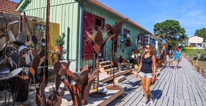 Um deck de madeira com esculturas de metal e um edifício verde com uma porta vermelha.