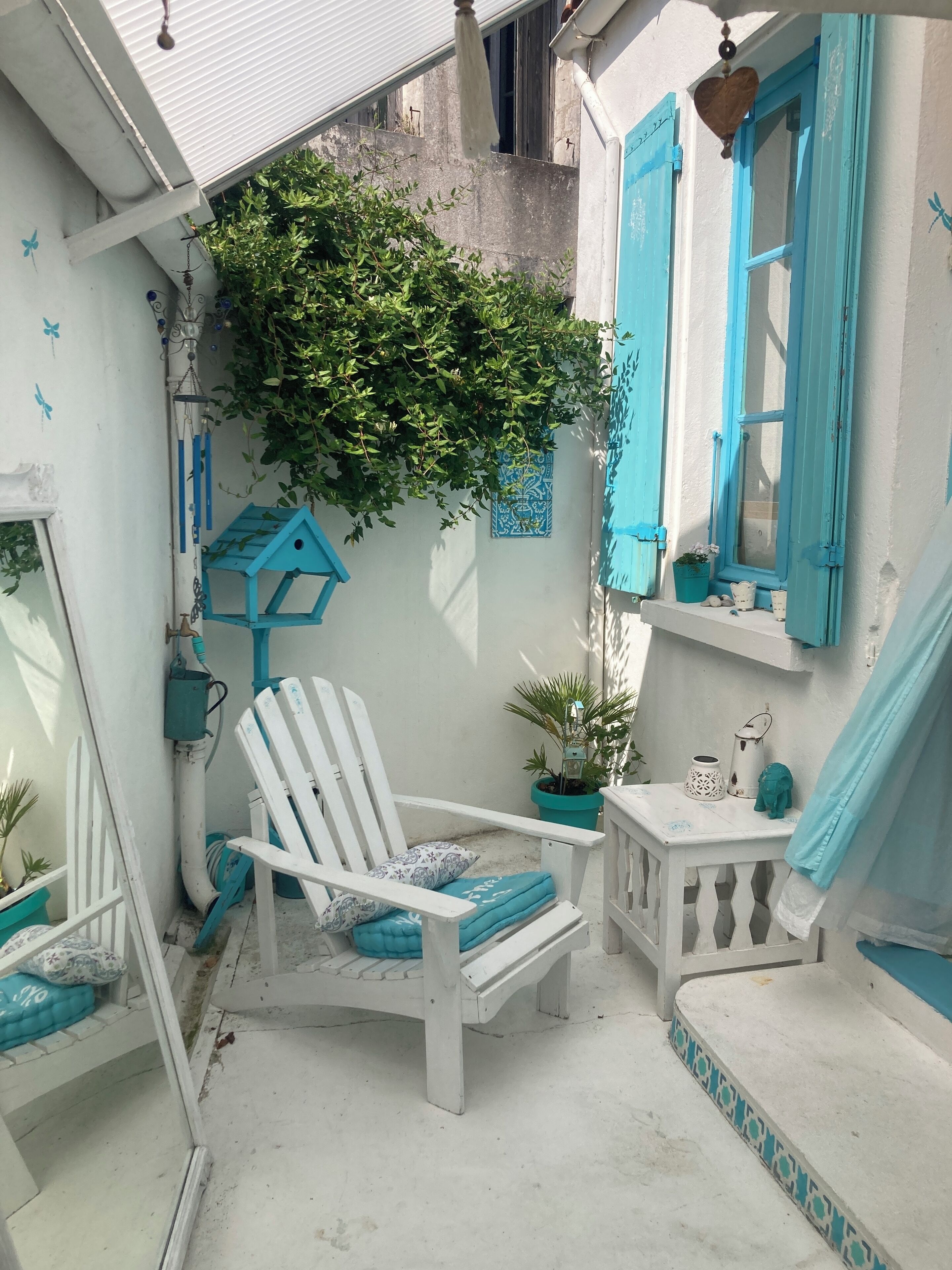 Un petit espace extérieur clos, comprenant une chaise blanche, une petite table et une plante en pot.