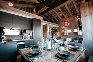 Una cucina moderna con mobili scuri, soffitto in legno e zona pranzo per sei persone, apparecchiata con piatti, bicchieri e un centrotavola a candela.
