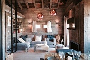 A cozy living room with a grey sofa, wooden beams, a fireplace, and a bear statue. - Chalet Dovakhiin Collection Perles (Bolquère)