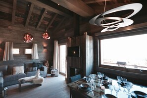 Un interno moderno con soffitto in legno, un camino, un tavolo da pranzo apparecchiato con bicchieri e un divano.