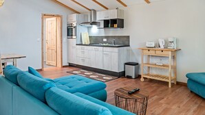 Un salon moderne avec un canapé bleu, une table basse et un coin cuisine doté de meubles en bois et d’un four encastré.