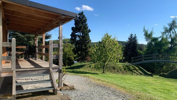 Un pavillon en bois doté d’un espace de repos couvert et d’un sentier de gravier menant à un pont enjambant un ruisseau.