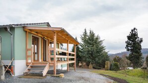 Une petite cabane en bois d’un seul étage, dotée d’un porche, d’une allée en gravier et bordée par une forêt.