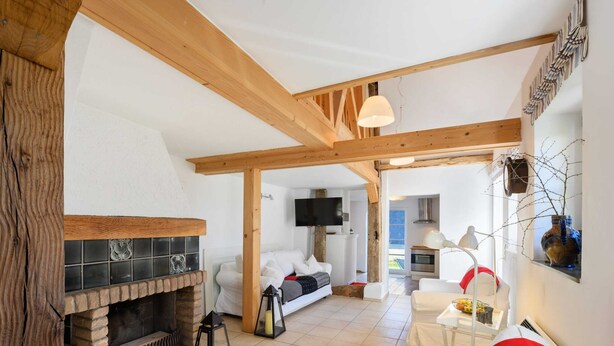 A cozy living room with a fireplace, wooden beams, a TV, and a dining area with a table and chairs. - Chalet in Korbach Nahe Skigebiet Willingen (Korbach)