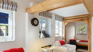 A cozy room with two white chairs, a small table with a lamp, and a bed with red and white bedding. - Chalet in Korbach Nahe Skigebiet Willingen (Korbach)