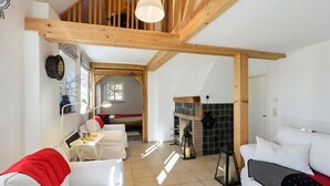 A spacious living room with high ceilings and exposed wooden beams, a fireplace, and a cozy seating area with white sofas and a red throw blanket. - Chalet in Korbach Nahe Skigebiet Willingen (Korbach)