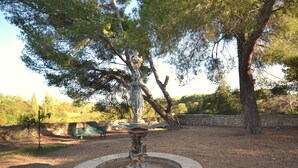 Un parque con una fuente, una estatua y un muro de piedra.