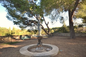 Un parc avec une fontaine, une statue et un mur de pierre.