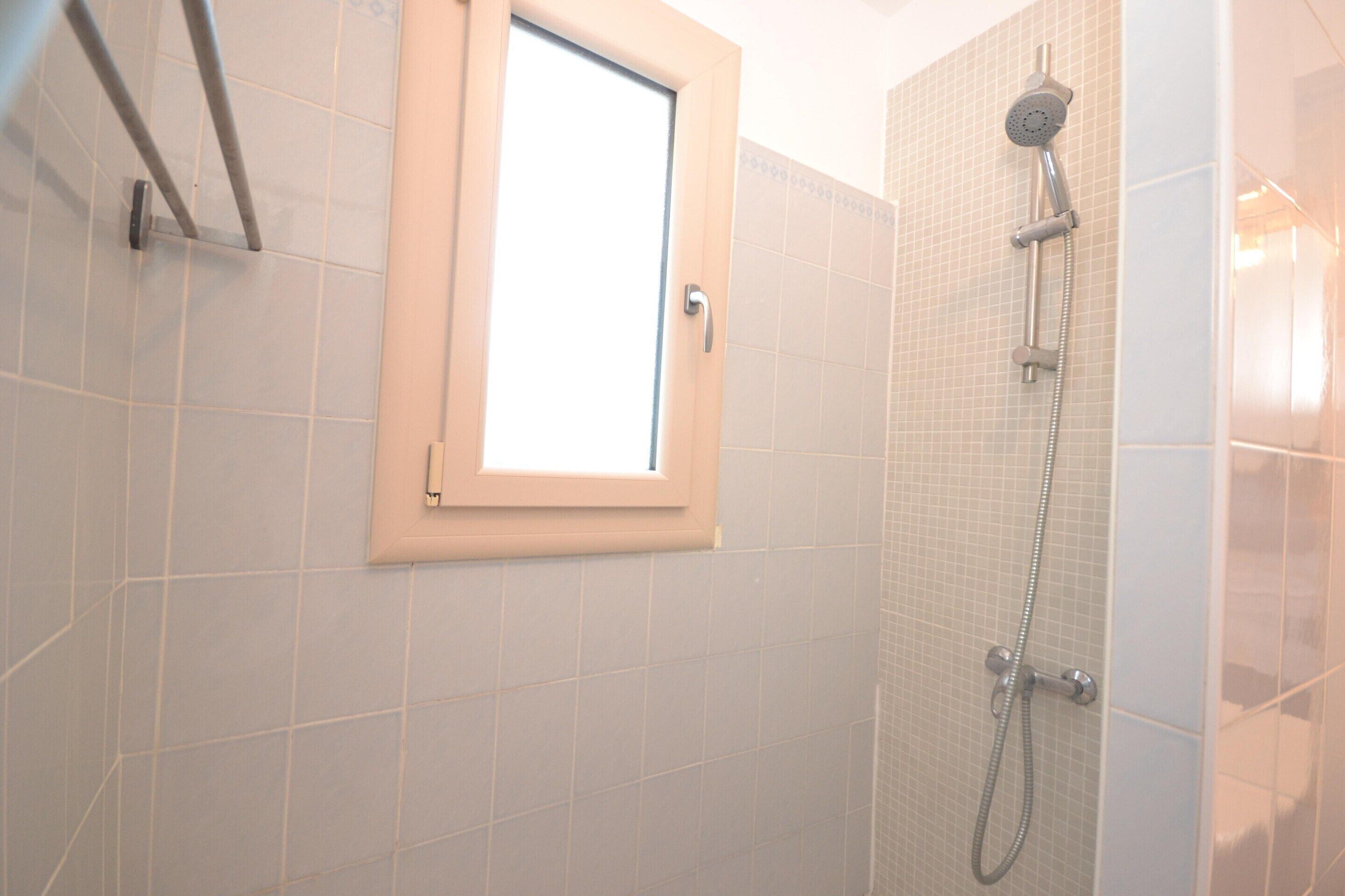 Ein Badezimmer mit Dusche, Fenster und gefliesten Wänden.