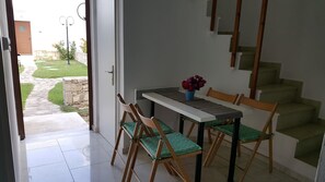 A dining area with a table and chairs, a vase with flowers, and a view of a garden through an open door. - Splendid Holiday Home With Swimming Pool (Rethymno)