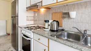 Una cuina amb armaris blancs, una placa de gas, una olla i un rentaplat.