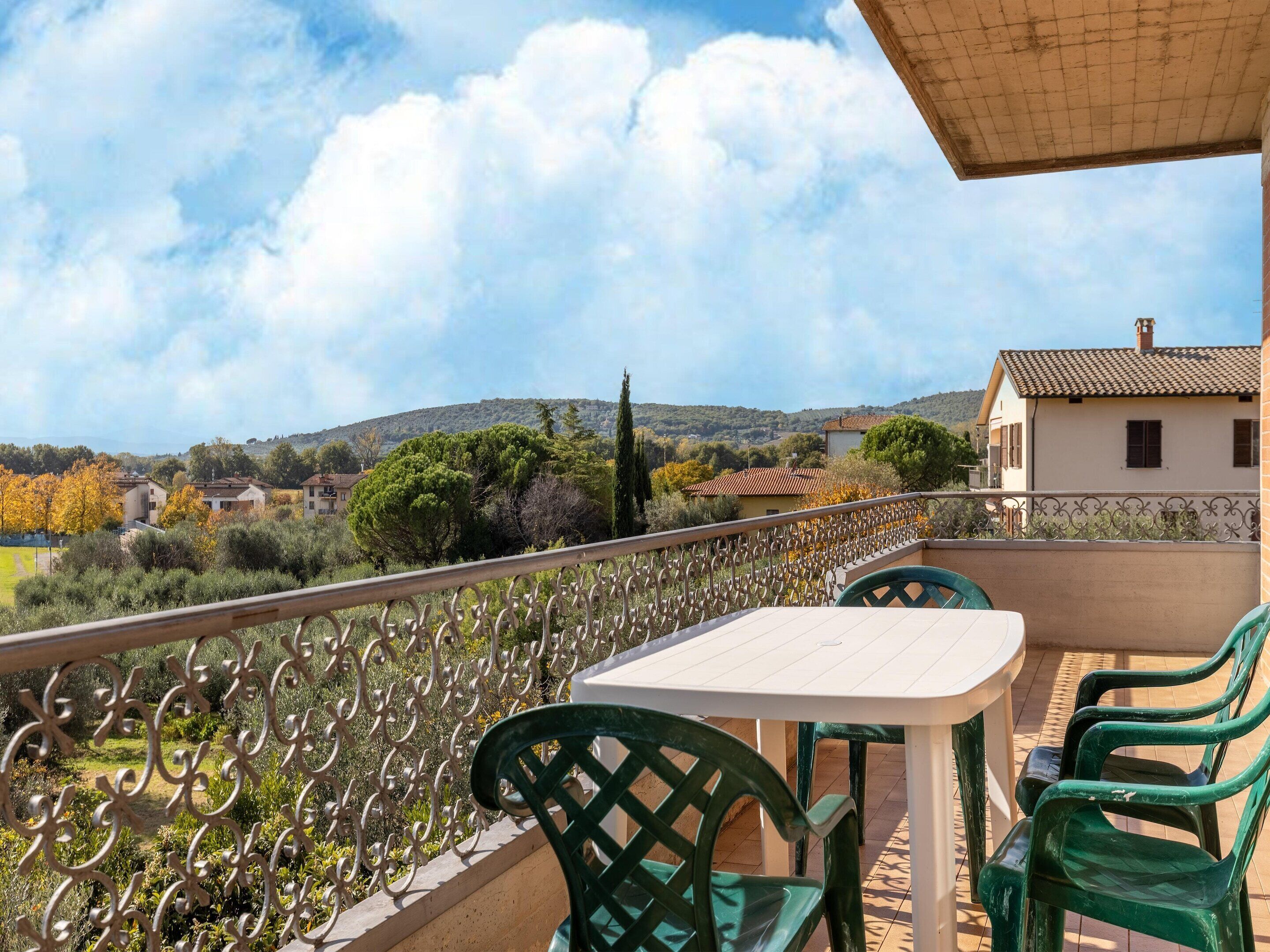 A balcony with a table and chairs, overlooking a scenic landscape with houses and trees.