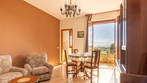 A living room with a dining table, two patterned sofas, a chandelier, and a balcony with a view. - Apartment in Tuoro Near Lake Trasimeno (Tuoro sul Trasimeno)