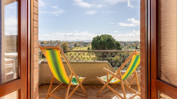A balcony with two wooden chairs and a metal railing, overlooking a rural landscape with houses and trees. - Apartment in Tuoro Near Lake Trasimeno (Tuoro sul Trasimeno)