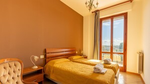 A hotel room with two beds, a wooden headboard, a chair, a nightstand, a lamp, and a view of the outdoors. - Apartment in Tuoro Near Lake Trasimeno (Tuoro sul Trasimeno)