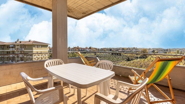 A balcony with a table and chairs, a colorful beach chair, and a view of a residential area. - Serene Lakeview Apartment (Tuoro sul Trasimeno)