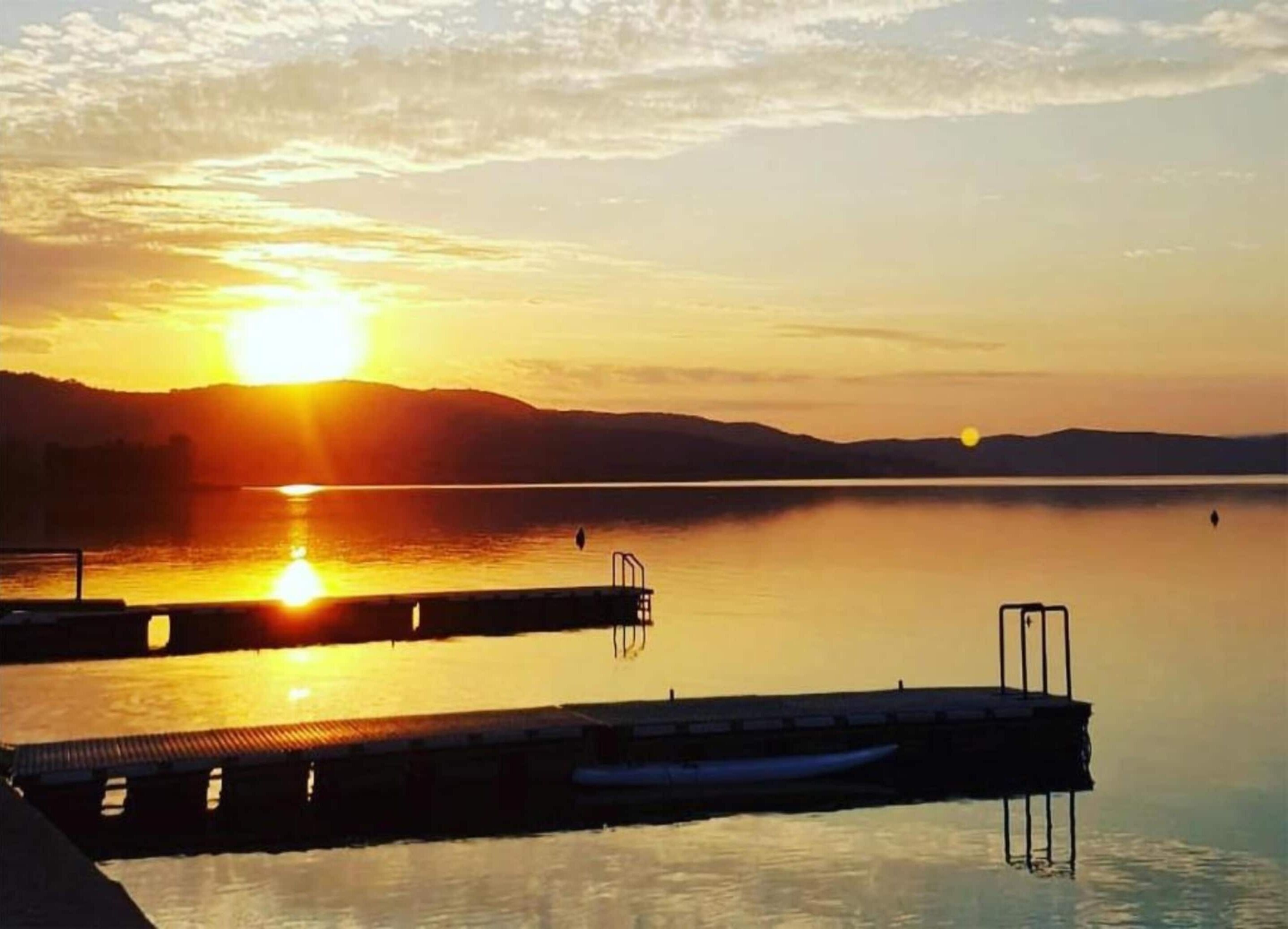 Un atardecer sobre un lago tranquilo, con un muelle que se adentra en el agua.