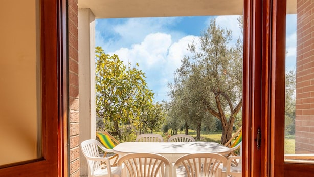A patio with a table and chairs, a brick wall, and a view of trees and sky. - Spacious Lakefront Apartment (Tuoro sul Trasimeno)