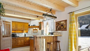 A spacious kitchen with wooden cabinets, a central island with stools, a hanging light fixture, and a painting on the wall.
