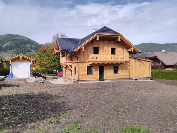 A wooden chalet with a balcony, a garage, and a small shed.