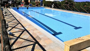 Piscina com deck revestido, cadeiras de descanso, guarda-sóis e vista para a paisagem ao redor.