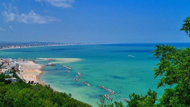 Vista costeira com praia, águas azul-claras e o skyline de uma cidade ao longe.