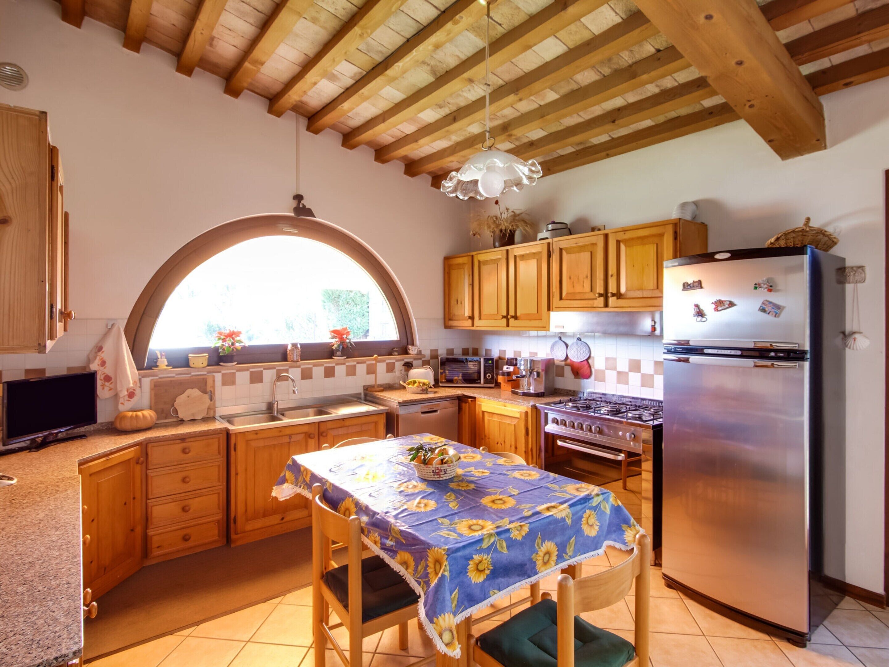 A kitchen with wooden cabinets, a stainless steel refrigerator, a stove, and a dining table with a sunflower tablecloth.