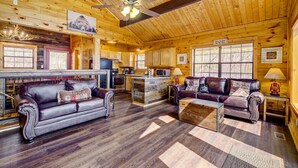 A log cabin interior with a fireplace, leather sofas, wooden floors, and a kitchen area. - Tennessee Chalet (Gatlinburg)